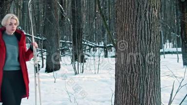 一个穿红色<strong>羽绒服</strong>的年轻女子把她的滑雪板放在森林里的树附近
