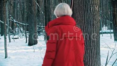 一个穿红色<strong>羽绒服</strong>的女人在树旁滑雪，然后向前走