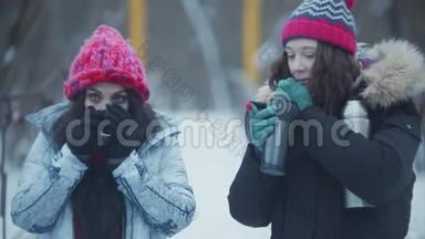两个年轻漂亮的女朋友走在雪桥上，<strong>喝</strong>着<strong>热水</strong>瓶里的热饮料