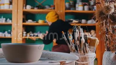 陶器车间-制作陶制碗碟的不同工具-<strong>一个人走</strong>到架子上，从架子上拿出油漆