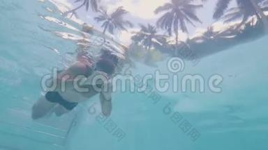 在热带棕榈背景下，在室外游泳池里游泳的年轻人在水下观看。 男子游泳者在度假泳池游泳