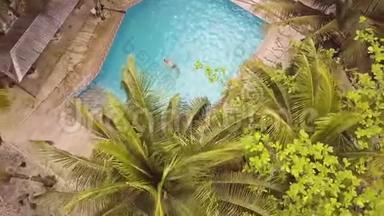 在热带酒店的蓝水漂浮游泳池里游泳的无人视野男子。 空中景观夏季平房和游泳