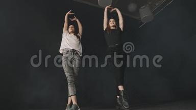 两个年轻漂亮的女人在黑暗工作室训练同步舞蹈编排