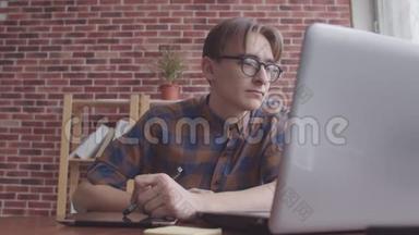这位网页设计师用一台带有平板电脑的笔记本电脑工作。 一个头发散乱的家伙用一个图形平板电脑