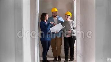 一位房地产经纪人向一对戴着黄色头盔的年轻夫妇展示了一套新的草稿公寓，上面有一个布局