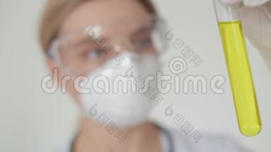 一个年轻的医学女孩戴着防护眼镜和医疗面罩，拿着一个黄色溶液的试管。 把一个
