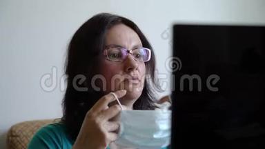 女人戴上面具，在笔记本电脑上读到关于病毒泛滥的新消息，看上去吓坏了，感到震惊和沮丧