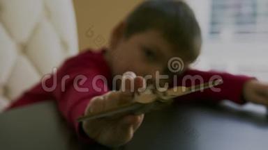 一个穿着红色毛衣的小男孩手里拿着一架玩具飞机的木制模型，和他在一张桌子