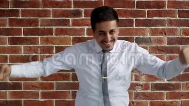 一个穿衬衫的人正在砖墙上跳舞。 快乐的阿拉伯企业家为胜利而欢欣鼓舞