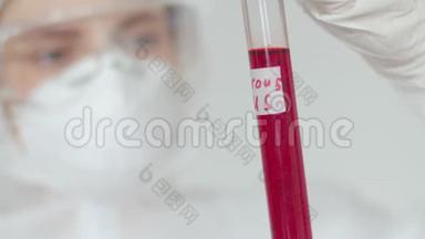 一位戴着化学<strong>防</strong>护、安全<strong>眼镜</strong>和口罩的妇女检查了一个带有危险病毒字样的红色试管
