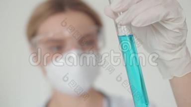 一个戴着<strong>防</strong>护<strong>眼镜</strong>和口罩的年轻医学女孩拿着一个试管，里面装有冠状病毒的解毒剂