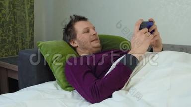 盖着毯子的人躺在<strong>床上玩手机</strong>游戏。 失眠观念，失眠.. 高加索人