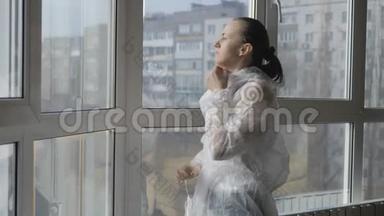 在大流行病毒<strong>时期</strong>，一名妇女穿着防护服，戴着面具站在窗边。