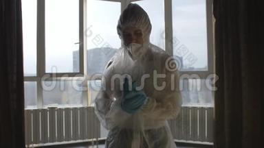 病毒感染的预防.. 站在窗边的女人穿着防护服和防护面罩。
