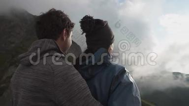 一对年轻幸福的夫妇拥抱着，站在山崖上向前看
