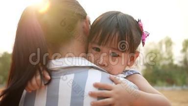亚洲母亲在夏天的公园拥抱她的女儿。 小孩子在田里跌倒时哭了. 概念
