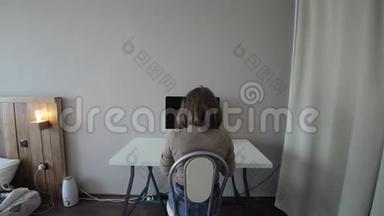 一个女孩坐在桌子前在电脑上工作的后视图。 特写