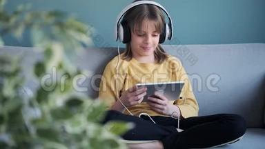 <strong>小女孩</strong>坐在家里的沙发上，一边用耳机和数字平板电脑<strong>听音乐</strong>。