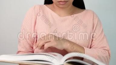 女人`翻书页，在图书馆看书时，她的手指沿着书页移动。 有选择的焦点。