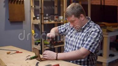 制作手工皮钱包的大师在制作皮孔的工具上<strong>敲打</strong>锤子。 双簧工作
