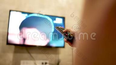 亚洲年轻女子在房间里看电视，手里拿着遥控器调节音量或更换<strong>电视频道</strong>。 在l中放松