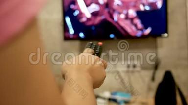 亚洲年轻女子在房间里看电视，手里拿着遥控器调节音量或更换电视频道。 在l中放松