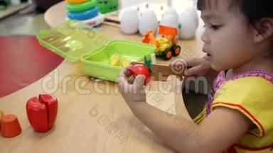 可爱的小女孩在教室的客厅玩烹饪玩具。 小孩用木头玩具刀切植物