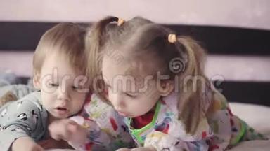 两个可爱的孩子躺在床上用蜡笔画画。女孩和男孩在床上玩铅笔。兄妹双胞胎