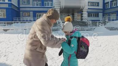 在学<strong>校门</strong>口的母女在冬天道别。 母亲纠正女儿`衣服