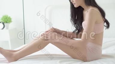 美丽的年轻亚洲女人用奶油和润肤露触摸皮肤的腿部光滑