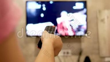 亚洲年轻女子在房间里看电视，手里拿着遥控器调节<strong>音量</strong>或更换电视频道。 在l中放松