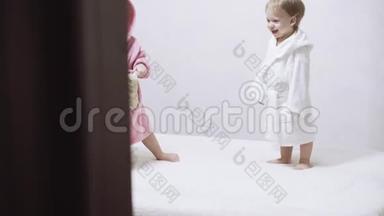 两个孩子穿着浴袍在一个白色背景和湿发后洗澡。 在白色床上洗澡后的男孩和女孩