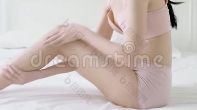 美丽的年轻亚洲女人用奶油和润肤露触摸皮肤的腿部光滑