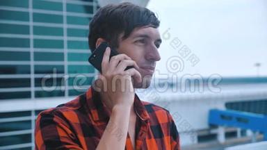 年轻人在机场大楼后台接电话。 在他的智能手机上聊天。 穿着红色格子衬衫。