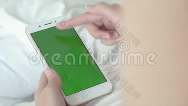 年轻女子躺着触摸和滑动绿色屏幕智能手机观看视频