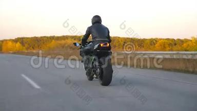 在秋天的高速公路上骑着现代摩托车的人面目全非。 摩托车手在乡下骑摩托车