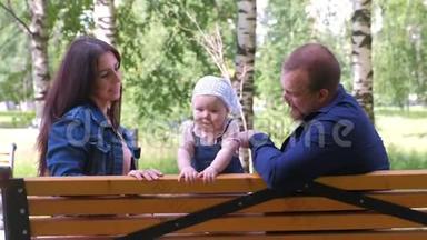 一家人爸爸妈妈和一个小女孩坐在城市公园的长椅上玩耍。
