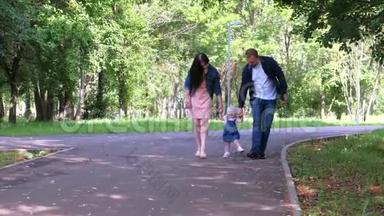 小女孩试图走第一步，牵着爸爸妈妈`手在城市公园。