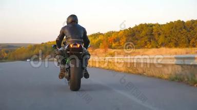 在秋天的高速公路上骑着现代摩托车的人面目全非。 摩托车手在乡下骑摩托车