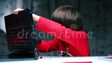 一个男孩坐在桌子旁检查笔记本<strong>电脑</strong>的<strong>背面</strong>。