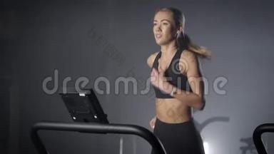 在健身房跑步机上滑溜溜的金发女郎。 一个身材漂亮，身材紧绷的女孩。 在健身房跑步。