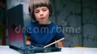 这个男孩坐在一张带着笔记本电脑的桌子旁，用铅笔把钥匙弄坏了。