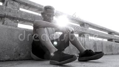 疲惫的亚洲老人在户外慢跑后坐在桥上的黑白色调。 健康的生活方式和保健理念..