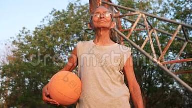 自信的亚洲老人穿着<strong>运动服</strong>，夏天在户外<strong>篮球</strong>场上拿着<strong>篮球</strong>。 健康的生活方式和方式