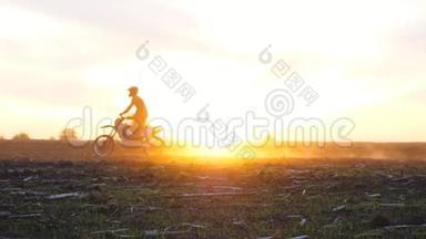 骑摩托车的人站在摩托车上穿过田野，对抗日落。 积极户外休息的朋友