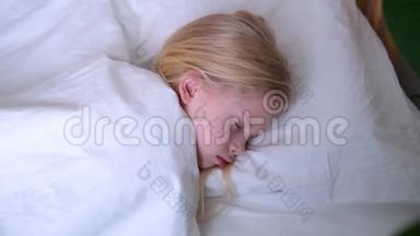 睡着的金发小女孩一大早就躺在大床上，铺着白色床上用品。 上景。 儿童梦