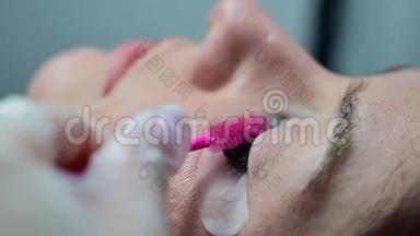 一个女人躺着，闭着<strong>眼睛做</strong>美容<strong>手术</strong>。 主人用粉红色的刷子梳理延伸的睫毛。