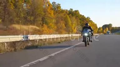 在秋高气爽的高速公路上骑着现代摩托车的年轻人。 摩托车手在乡间公路上骑摩托车