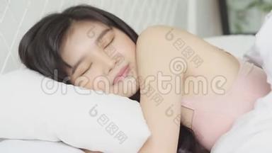 美丽的亚洲年轻女子躺在床上，头靠在枕头上，舒适而快乐地躺在卧室里