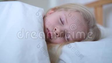 睡着的金发小女孩一大早就躺在大床上，铺着白色床上用品。 孩子们做梦。 童年，平静